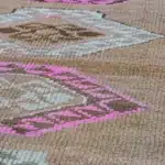 Close-up of a tan rug with pink and brown diamond medallion weave.