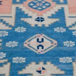 Folded corner of a rug showing blue, pink, and cream tribal motifs